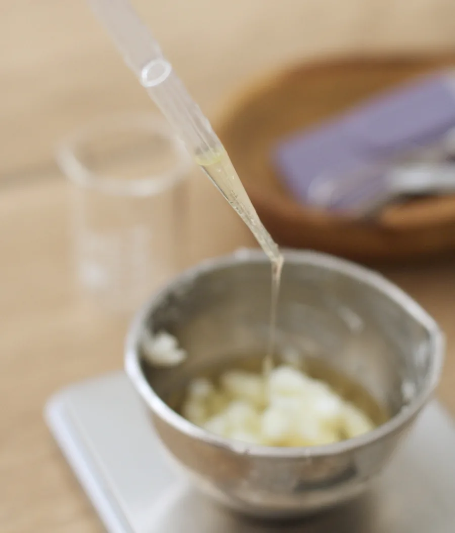 Une pipette laisse tomber un filet d’huile dans un bol d’acier posé sur la balance